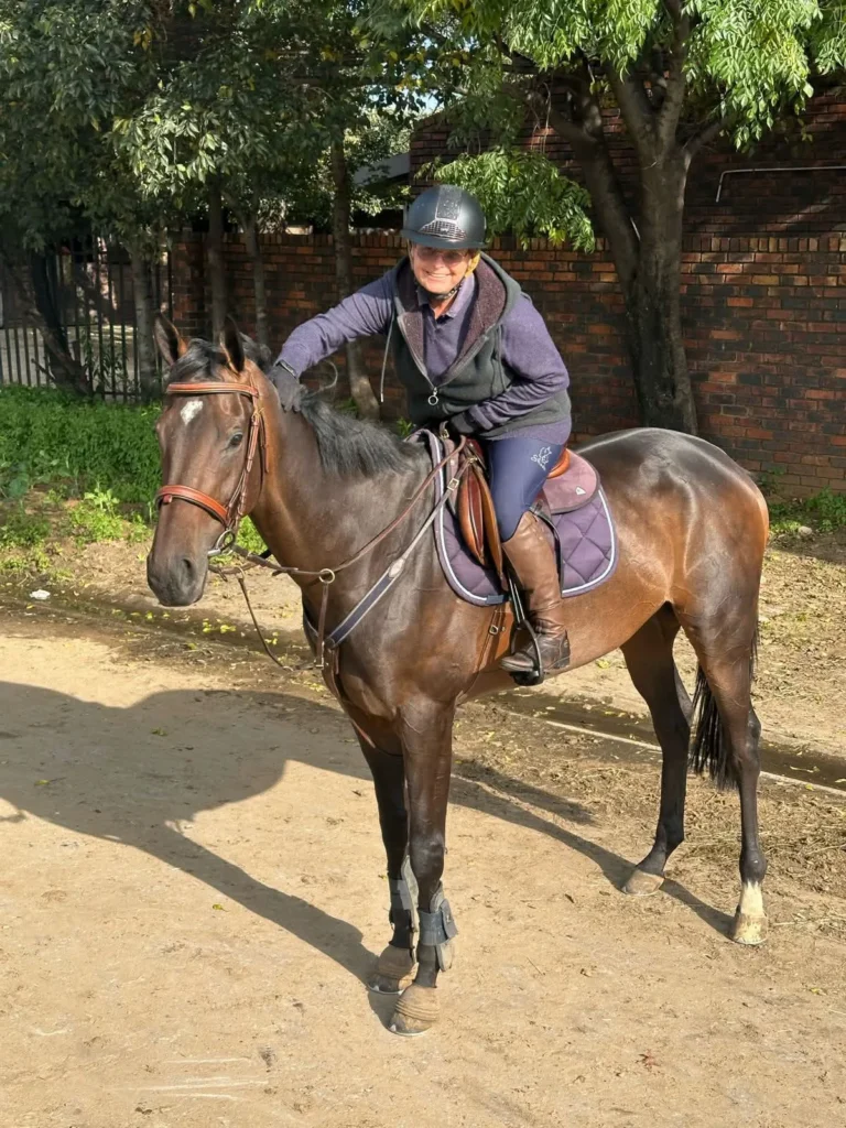 A rider on a horse reaching and leaning forward to pet her horse on it's head happily.