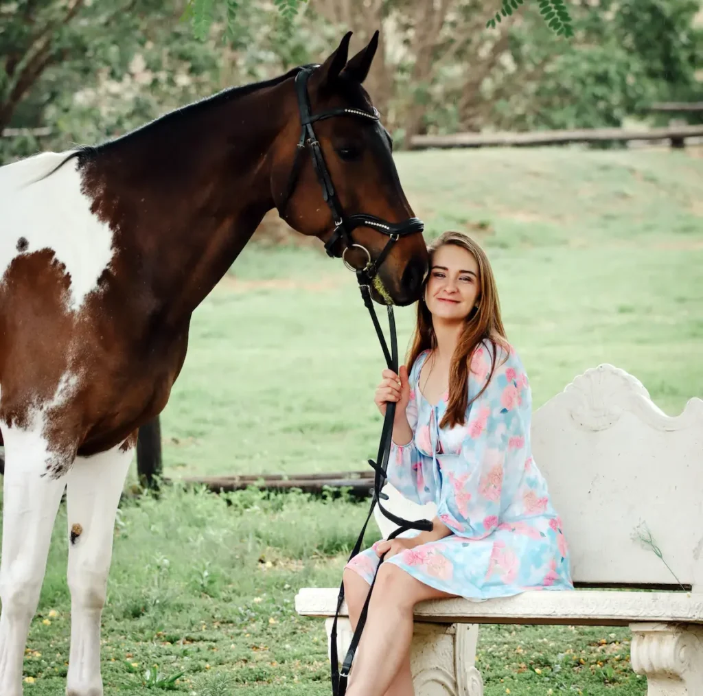 Sherize sitting on a bench in a picturesque field with her horse next to her